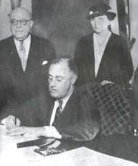 President Roosevelt signing the National Labor Relations Act into law on July 5, 1935, with Labor Secretary Frances Perkins looking on.